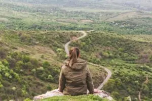 woman sitting on ledge overlooking a valley and path
